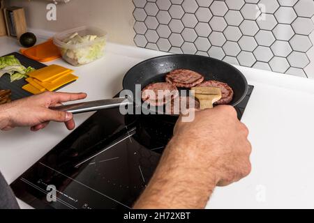 Les mains des jeunes hommes cuisent des hamburgers de bœuf dans une poêle antiadhésive Banque D'Images