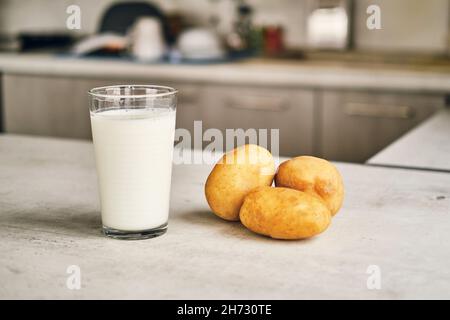 Un verre transparent avec du lait de pomme de terre sur la table à côté des tubercules de pomme de terre. Banque D'Images