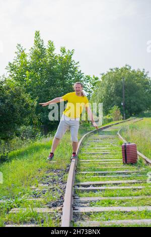 un voyageur seul avec une valise rouge marche sur les rails Banque D'Images