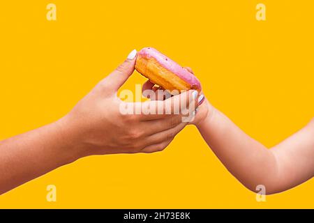 la main femelle passe un donut rose délicieux à la main d'un enfant. livraison Banque D'Images