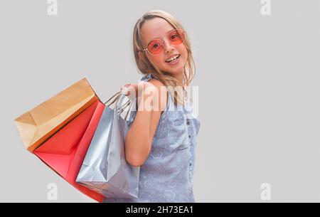 Enfant avec des lunettes sur fond gris. Fille tenant des sacs à provisions Banque D'Images