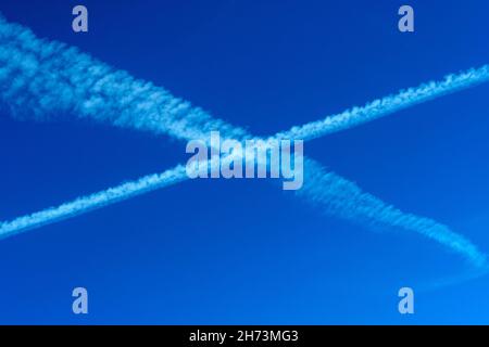 Les traînées se croisent dans un ciel bleu clair pendant la journée, créant un motif complexe au-dessus du paysage Banque D'Images