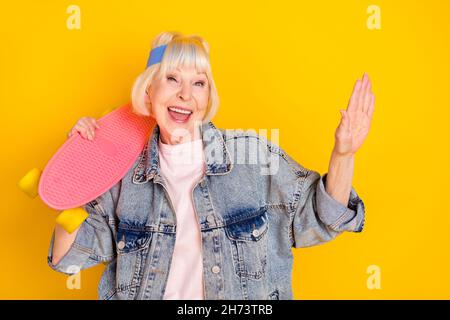 Portrait d'une jolie femme gaie et funky ayant l'amusement dansant tenant le skate isolé sur fond jaune vif Banque D'Images