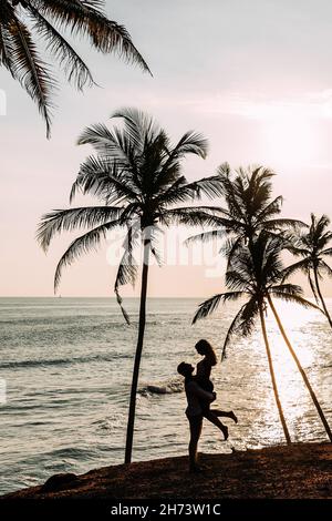 Un couple amoureux rencontre un coucher de soleil sur la mer parmi les palmiers.Homme et femme au coucher du soleil.Lune de miel sur les îles.Voyage de noces.Coupé joyeux Banque D'Images