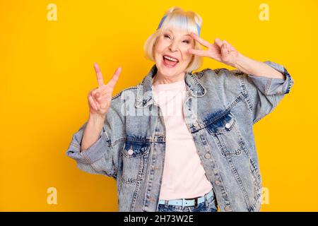 Portrait de la femme joyeuse attrayante et joyeuse ayant l'amusement montrant le V-signe dupe isolé sur fond jaune vif de couleur Banque D'Images
