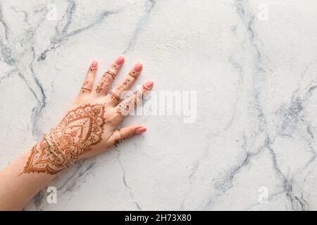 Femme avec des mains peintes au henné dans des bagues et des bracelets sur fond de marbre clair Banque D'Images