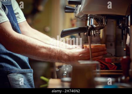 Un barman utilise un appareil à espresso derrière le bar pour préparer un café aromatique et parfumé.Café, boissons, bar Banque D'Images