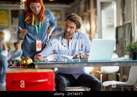 jeune employée de redhead expliquant les données statistiques dans le document à un patron d'âge moyen de beardy, qui analyse le rapport. Banque D'Images