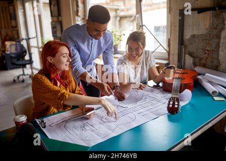 Un groupe de jeunes collègues créatifs dans une atmosphère de travail au bureau apprécie de travailler ensemble sur une nouvelle conception de guitare Banque D'Images