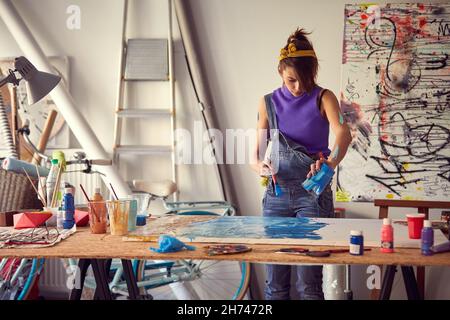 Une jeune artiste verse la peinture sur toile dans une atmosphère agréable dans son studio.Art, peinture, studio Banque D'Images