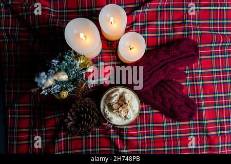 Une tasse de café avec crème et cinammon et petit arbre de Noël, cône de pin, bougies et moufles rouges Banque D'Images