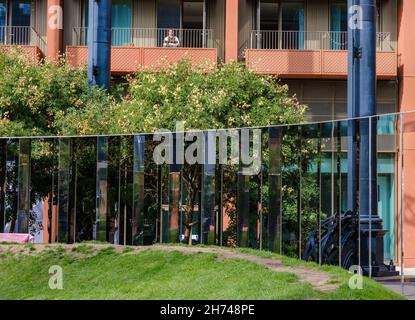 Le bord du parc Gasholder, avec la colonnade miroir et les appartements Gas Holder en arrière-plan avec un homme assis sur un balcon. Banque D'Images