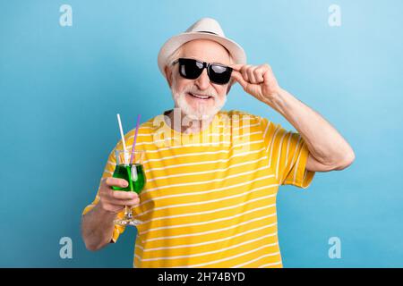 Photo de drôle cool age gentleman porter un t-shirt jaune chapeau lunettes sombres souriant tenant le cocktail isolé couleur bleu arrière-plan Banque D'Images