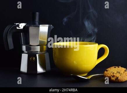 Moka pot, tasse jaune avec une boisson chaude, et biscuit dans le fond sombre Banque D'Images