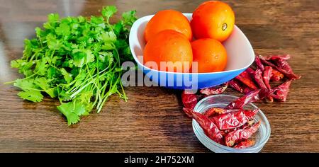 Quelques légumes, tomates Coriander et piments rouges entiers, pour faire du chutney et de la sauce sur une table en bois Banque D'Images