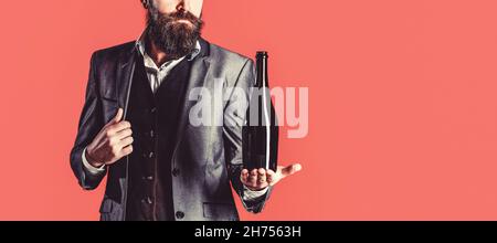 La personne tient une bouteille de vin rouge dans une main. Homme tenant une bouteille de champagne, vin. Homme barbu avec une bouteille de champagne et un verre Banque D'Images