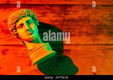 Copie en gypse de l'ancienne statue Hermès tête dans lumière orange vert néon.Image de néon avec la sculpture grecque ancienne tête Hermes.Concept d'art fantaisie minimal Banque D'Images