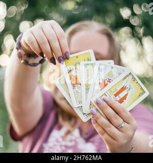 Les mains de femmes avec bracelet et clous violets tiennent le ventilateur des cartes de tarot face et de toucher l'un d'eux.Minsk, Bélarus, 28.07.2021 Banque D'Images