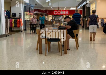 Townsville, Queensland, Australie - novembre 2021 : un homme assis à table dans l'allée du centre commercial pendant que les acheteurs marchent autour de lui Banque D'Images