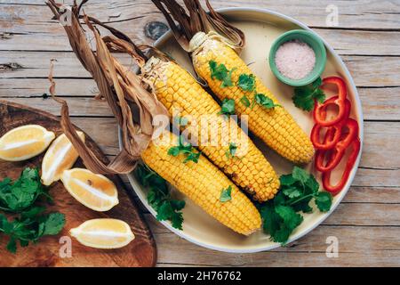 Épis de maïs cuits à la coriandre, tranches de poivron, citron et sel sur une table en bois.Cuisine mexicaine.Vue de dessus, plan d'appartement. Banque D'Images