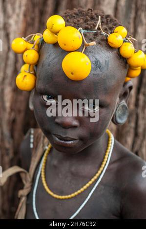 Jeune fille de la tribu Mursi en Ethiopie avec des fruits jaunes sur sa tête et de grands bouchons d'oreille Banque D'Images