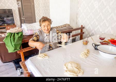 Une femme kazakh âgée préparant des nouilles longues en pool pour cuisiner un plat laghman, un repas traditionnel d'Asie centrale Banque D'Images