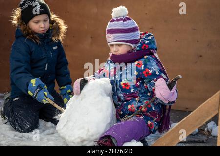 Un garçon et une fille jouent avec de la neige et font une boule de neige dans la rue. Banque D'Images