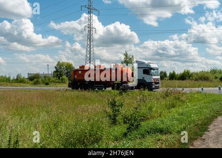 Un camion-citerne à essence avec un camion-citerne à essence orange et une inscription en russe - dangereux, se trouve sur la route par une belle journée d'été. Banque D'Images