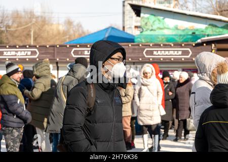 Un jeune homme d'origine asiatique se tient dans un masque de protection médicale parmi une foule de personnes sans masque sur une rue de ville au printemps. Banque D'Images