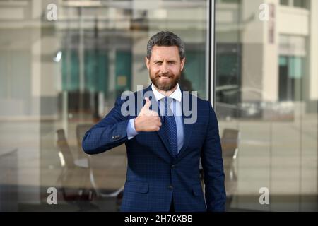 Un homme d'affaires souriant et souriant se fait des pouces.Un homme d'affaires qui se trouve près du bureau. Banque D'Images