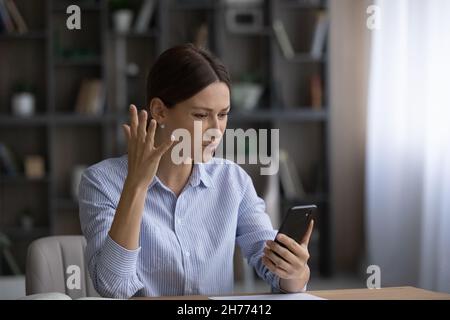 Une femme d'affaires ayant des problèmes avec un téléphone portable se sent agacée s'asseoir à son bureau Banque D'Images