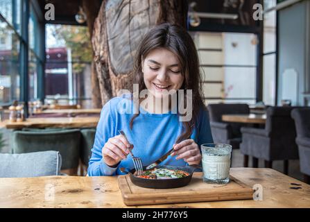 Une jeune femme dans un café dines sur le shakshuka traditionnel et ayran. Banque D'Images