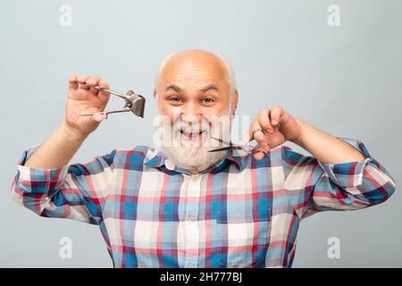 Ancien coiffeur.Joyeux vieil homme barbu, barbu avec ciseaux et tondeuse droite à cheveux de rasoir. Banque D'Images