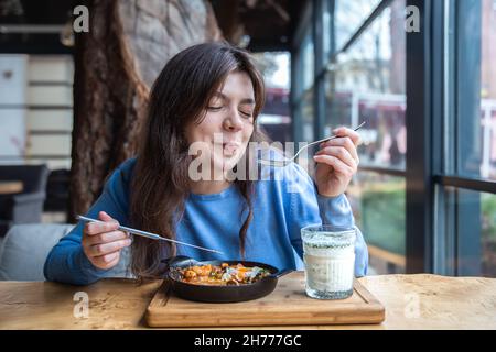 Une jeune femme dans un café dines sur le shakshuka traditionnel et ayran. Banque D'Images