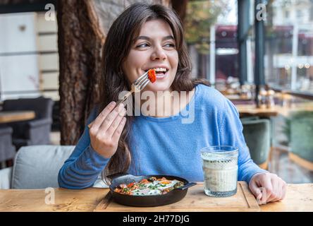 Une jeune femme dans un café dines sur le shakshuka traditionnel et ayran. Banque D'Images