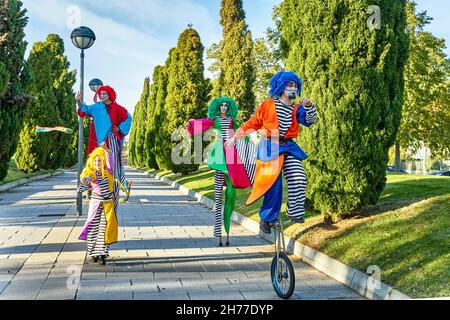 Troupe d'artistes créatifs drôles en costumes et perruques colorés, en marchant sur des pilotis et en monocycle pendant la parade le jour ensoleillé dans le parc Banque D'Images