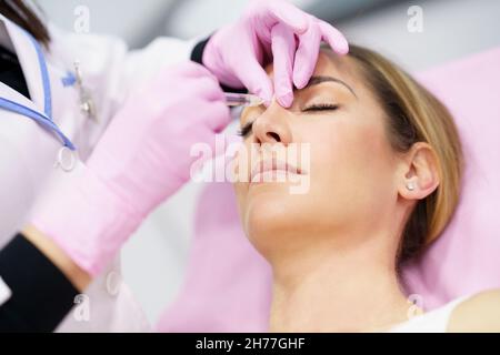 Médecin effectuant la rhinoplastie par injection d'acide hyaluronique dans le nez de son patient. Banque D'Images