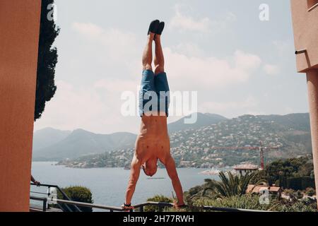 Un homme sportif se tient sur les mains à l'envers contre la vue sur la mer de France Banque D'Images