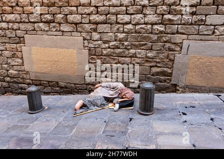 Une femme âgée mendiant attend pendant qu'elle se repose au bord d'une ruelle étroite dans le centre-ville de Barcelone, la Catalogne, l'Espagne, l'Europe. Banque D'Images