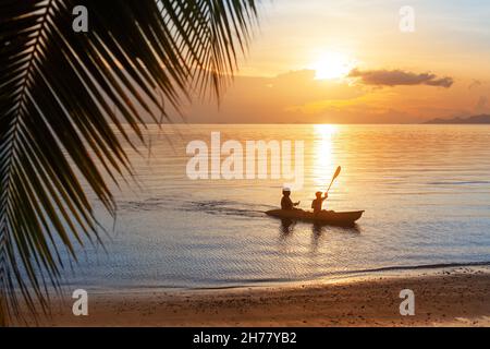 Coucher de soleil sur la mer, lever du soleil sur l'océan, plage d'îles tropicales, feuilles de palmiers, vague d'eau bleue,silhouette de deux personnes en bateau, kayak ramer, canoë sport Banque D'Images