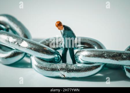 Photo macro d'une figurine d'homme d'affaires réfléchie debout dans un anneau de chaîne.Faillite d'entreprise, faillite, chômage concept.Chômeurs stressés Banque D'Images