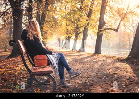 Détente dans le parc d'automne.Femme assise et reposant sur un banc dans un parc public.Été indien en ville Banque D'Images