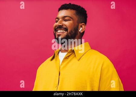Homme à l'écoute de son podcast préféré.Un jeune homme heureux souriant gaiement tout en portant des écouteurs sans fil dans un studio.Jeune homme insouciant debout un Banque D'Images