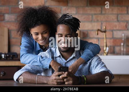 Heureux couple biracial utilisant des applications pour smartphone à la maison. Banque D'Images