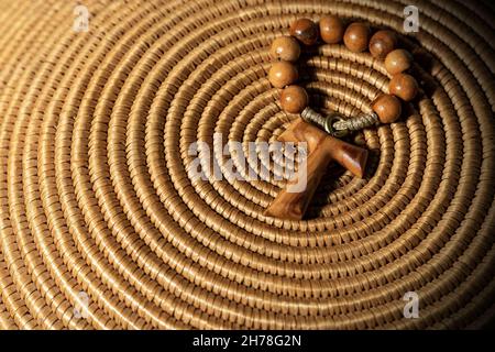 Tau, croix en bois en forme de lettre t (symbole religieux de Saint François d'Assise) à perles rosaces, sur une texture en osier brun tissé Banque D'Images