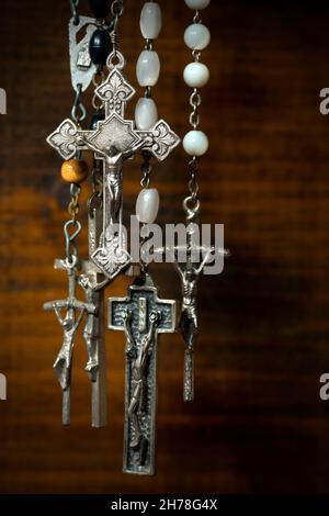 Détail d'un groupe de crucifix d'argent avec perles rosaires.Suspendu sur un arrière-plan en bois avec des ombres sombres Banque D'Images