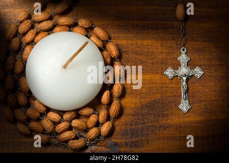 Vieux crucifix et rosaire argentés avec perles en bois et bougie votive blanche (lampe à thé).Sur fond en bois Banque D'Images