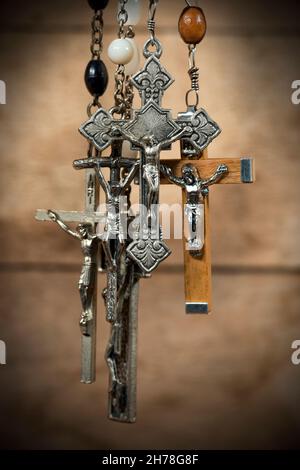 Détail d'un groupe de crucifix d'argent avec perles rosaires.Suspendu sur un arrière-plan en bois avec des ombres sombres Banque D'Images