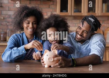 S'occuper de jeunes parents afro-américains enseignant petite fille économiser de l'argent, Banque D'Images