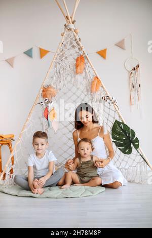 Jeune famille heureuse mère aimante avec deux enfants assis ensemble dans le tipi de wigwam à la maison, maman jouant avec un garçon et un tout-petit dans la tente de jeu, ver Banque D'Images